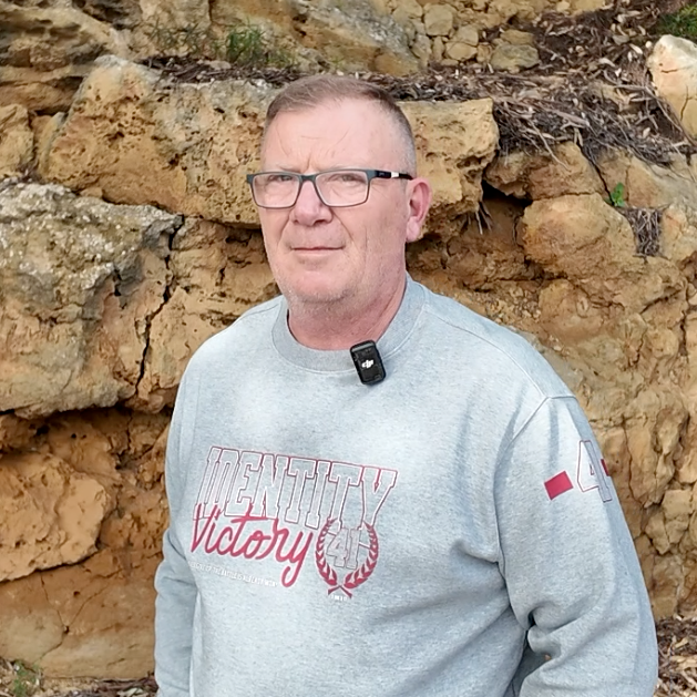 Man wearing a gray sweatshirt with 'Victory' text standing in front of a rocky wall.